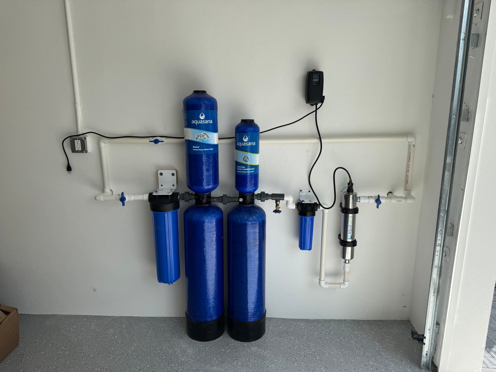Whole-house Aquasana water filtration system with carbon filtration tanks and UV sterilizer installed in a garage utility wall