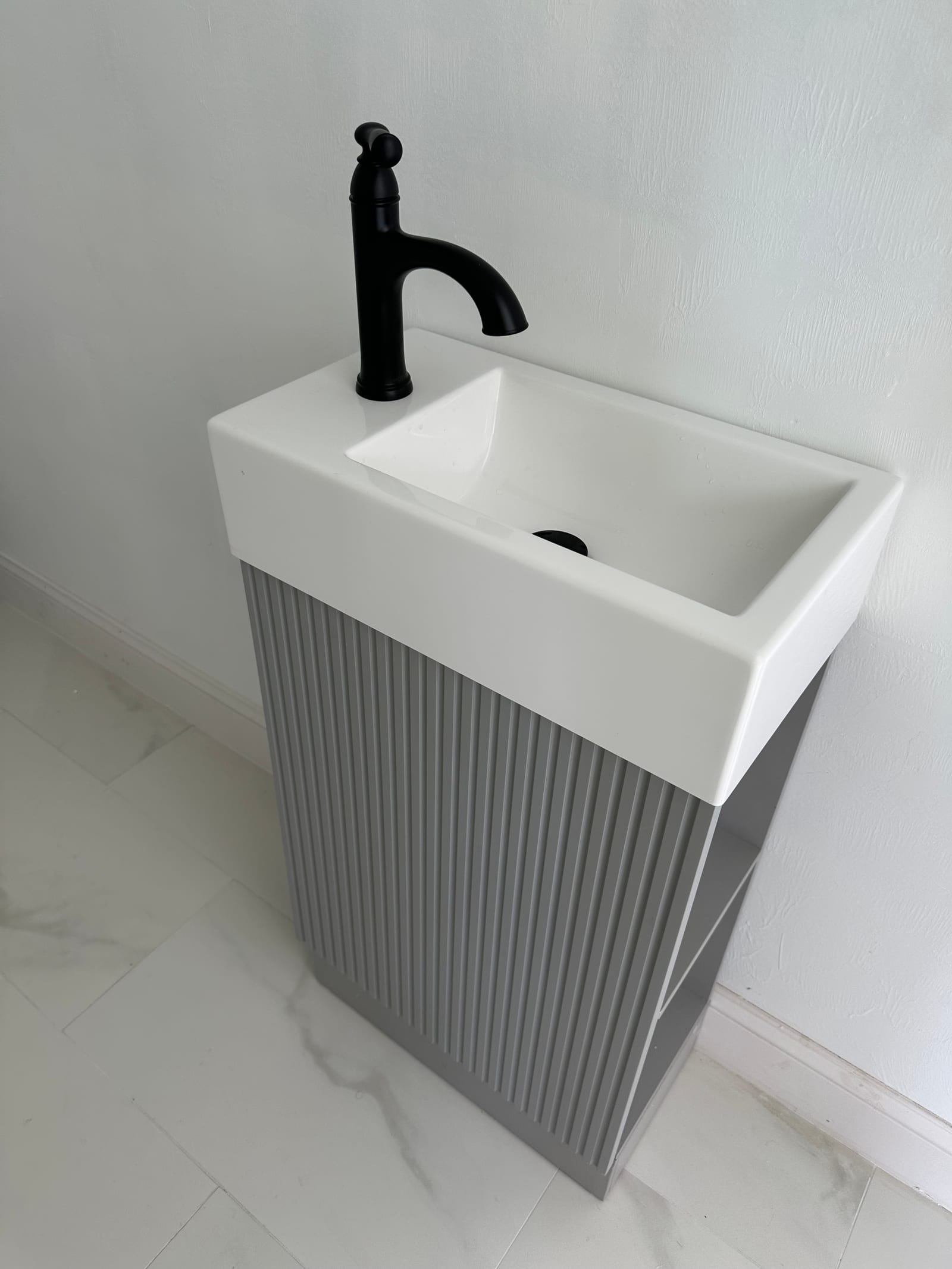 Compact wall-mounted ceramic vessel sink with matte black bridge faucet on a fluted gray pedestal