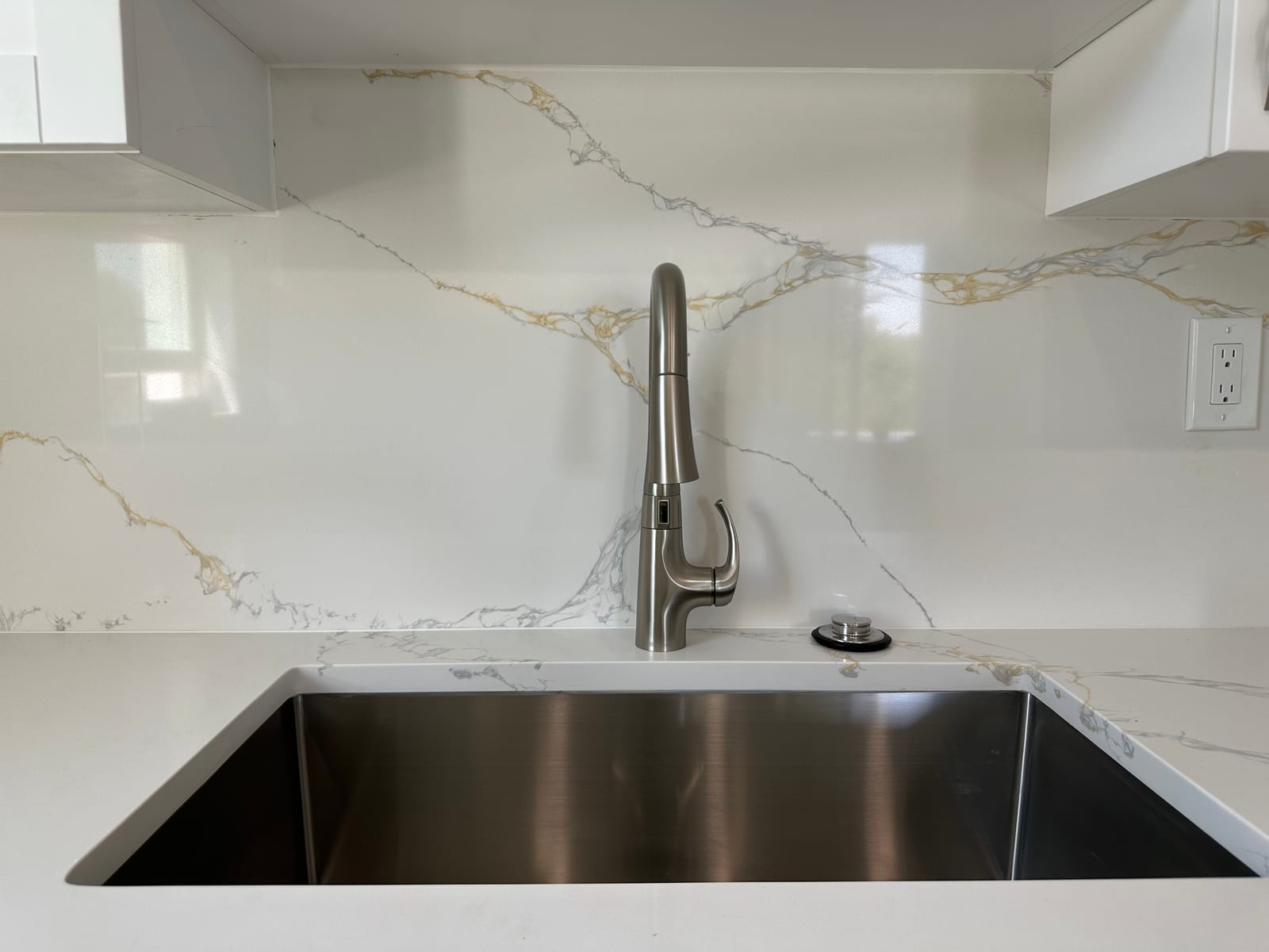 New stainless-steel undermount kitchen sink with brushed nickel pull-down faucet against marble-veined quartz
