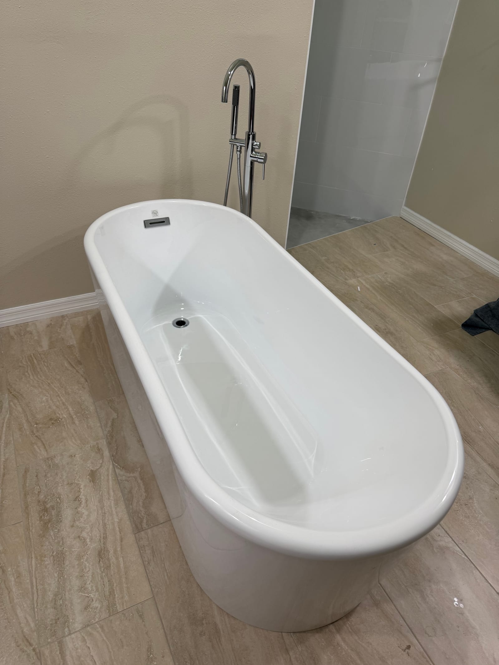 Freestanding slipper-style soaking tub with chrome floor-mounted tub filler and handheld in a newly remodeled bathroom