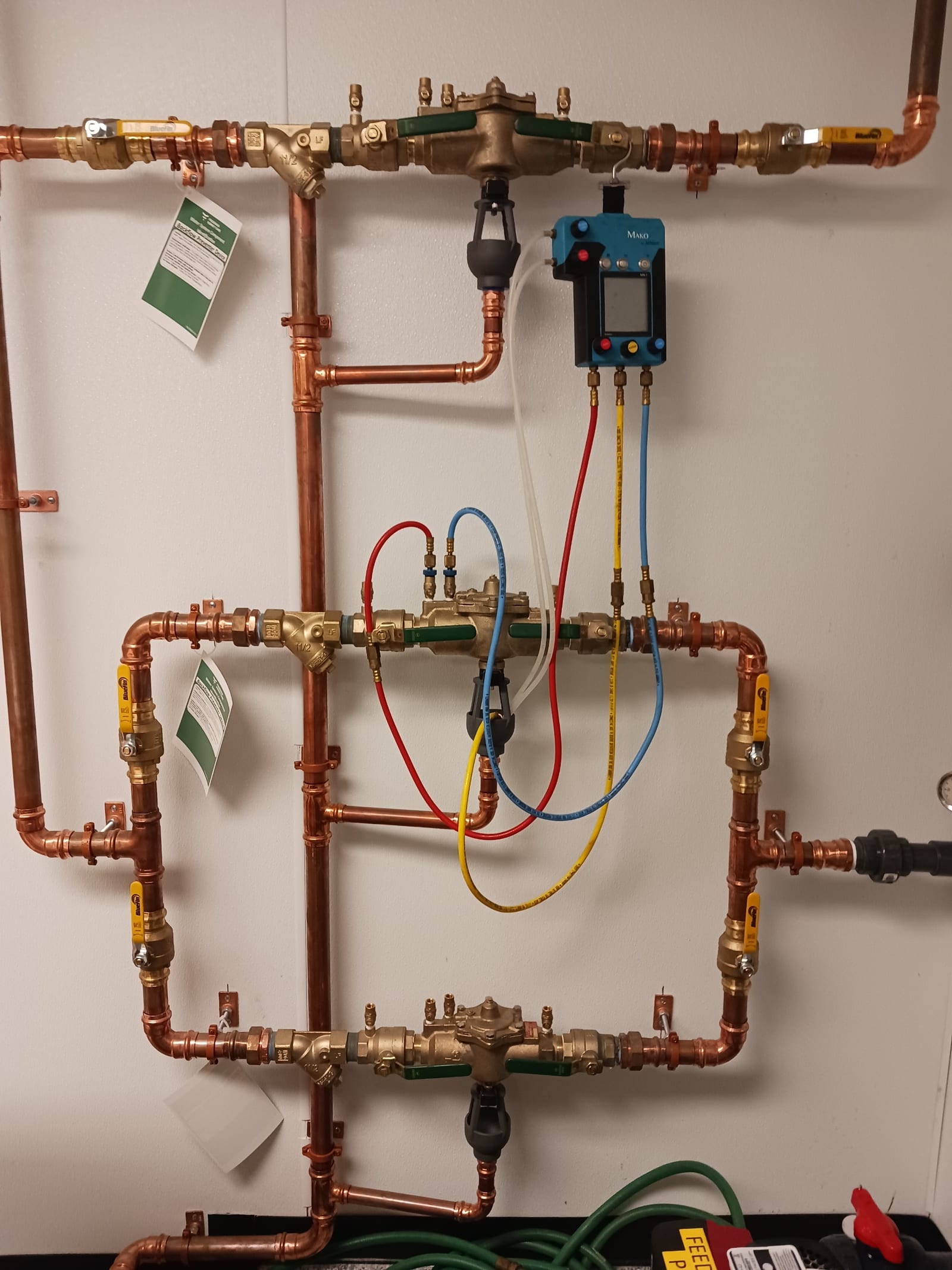 Backflow assembly testing in progress with digital test gauge connected to copper-piped backflow preventers