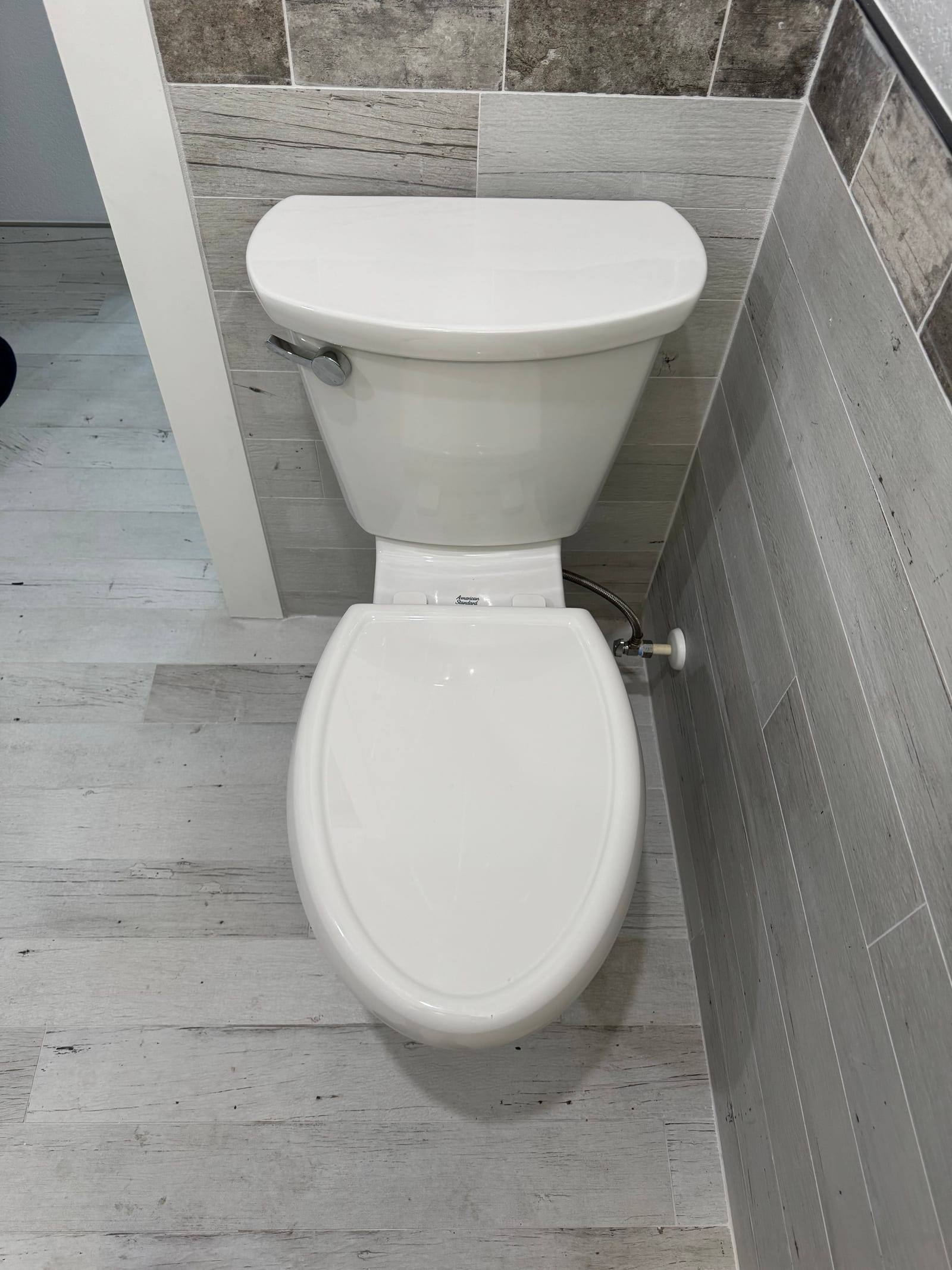 Newly installed elongated two-piece toilet in a remodeled bathroom with plank-tile accent wall