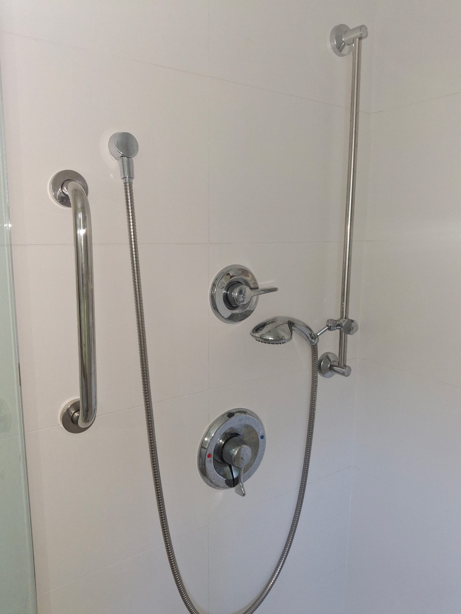 Accessible shower retrofit with chrome thermostatic valve, handheld on a slide bar, and stainless grab bar
